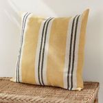 Pillow propped upright on woven wicker surface against off-white wall in bright light