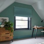 Wallpaper in a room with slanted ceiling, styled with wooden furniture and a color-matched blue roller blind