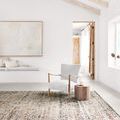Rectangular view of rug styled in a bright room with wooden beams, neutral chair, and small wood side table