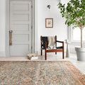 Layla Ocean Rust Rug displayed in a bright entryway with wooden chair, light gray door, and large leafy plant
