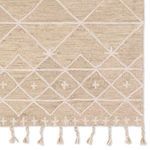 Close-up focusing on ivory trellis pattern with small plus shapes near edge and tasseled border