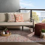 Patio setting with rug featuring distressed floral pattern under white cushion sofa and dark wood deck