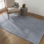 Rug styled flat on wood floor next to chair with gray throw and round side table