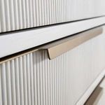 Close-up of matte brass drawer handle over ribbed white wood drawer front