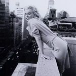 Close-up crop of Marilyn Monroe’s smiling face and upper body leaning on the rooftop ledge