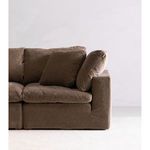 Side view of right armrest and cushions on dark brown fabric sofa against white wall