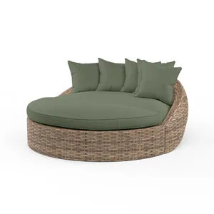 Round outdoor daybed in aged tobacco wicker with plush olive green cushions and multiple pillows