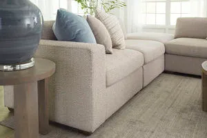 Corner sofa with textured oatmeal performance fabric and square arms accented by blue and beige throw pillows