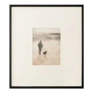 Framed print of man and dog walking on misty shore in earthy tones with black wood frame and textured matte