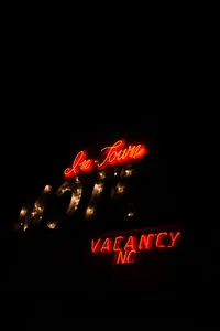 No Vacancy neon sign glowing in red and white lights against a black background, vintage motel style