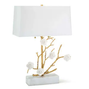 Table lamp with luxe gold cast metal branches and white porcelain flowers on a rectangular marble base and white rectangul...