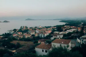 A serene coastal marina scene with red-tiled roofs on hillside and calm sea at dusk under pale sky