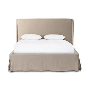 Beige linen slipcovered bed with tufted headboard, oversized welt edge, and kick pleat footboard