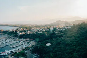 Warm sunset over Sardinia coast with Mediterranean boats, lush green hills, and distant hazy mountains
