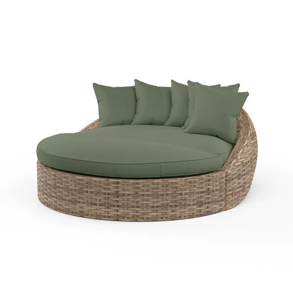 Round outdoor daybed in aged tobacco wicker with plush olive green cushions and multiple pillows