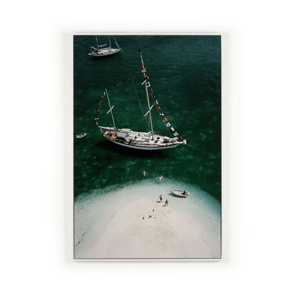 Aerial view of a classic charter ketch yacht anchored near a small white sand island with a few people and two small boats...