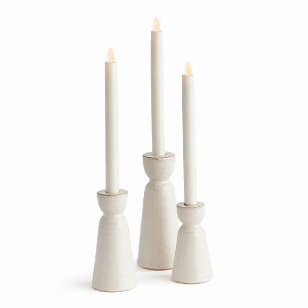 Three off-white stoneware taper holders with dynamic reactive glaze, varying in height, each holding a white taper candle