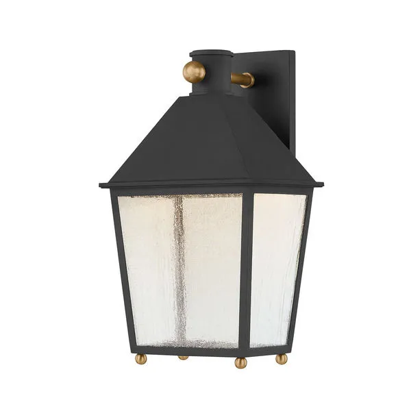 Lantern-style wall sconce in textured black with rippled seeded glass panels and patina brass ball accents