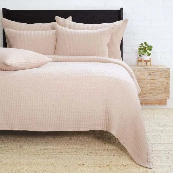 Amber-colored Vancouver Coverlet laid on queen bed with matching pillows and textured woven fabric