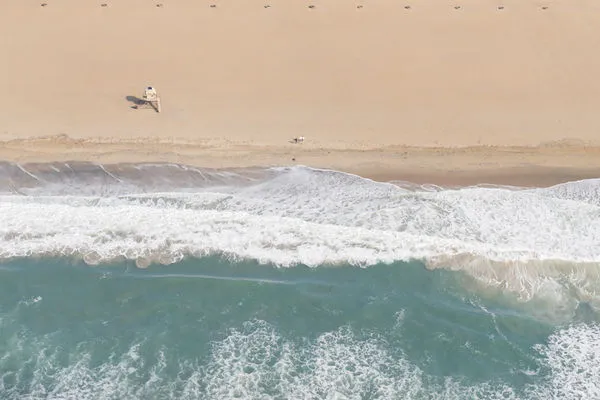 aerial view of a sandy beach with gentle ocean waves washing onto shore and a lone lifeguard chair