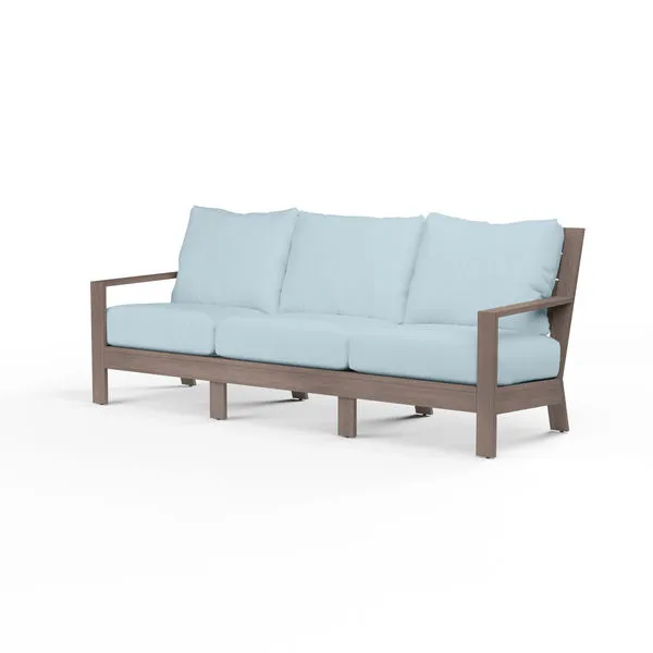 Laguna Sofa with driftwood-finish aluminum frame and light blue cushions, featuring plank arms and curved slat back