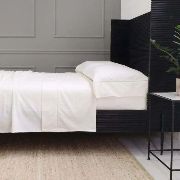 Ivory cotton sateen pillowcases with ladder stitch detail on a bed in a modern bedroom setting