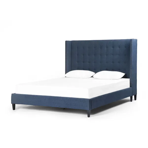 High shelter-back king bed upholstered in rich indigo twill linen with button tufting and brass nailhead trim