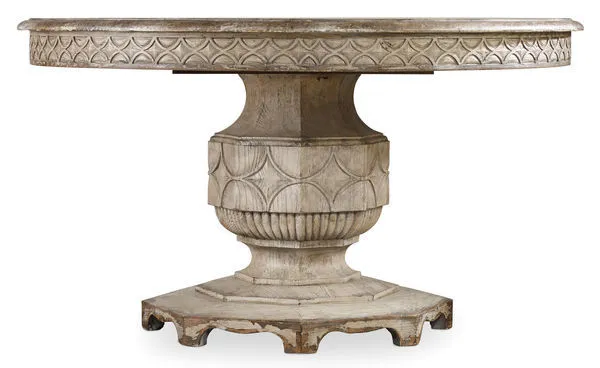 Round wooden dining table with scallop motif fretwork on apron and pedestal base, distressed light finish