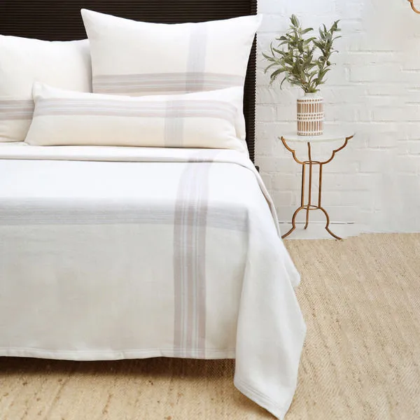 Geneva Blanket in muted plaid pattern with soft combed cotton draped over bed with pillows and side table