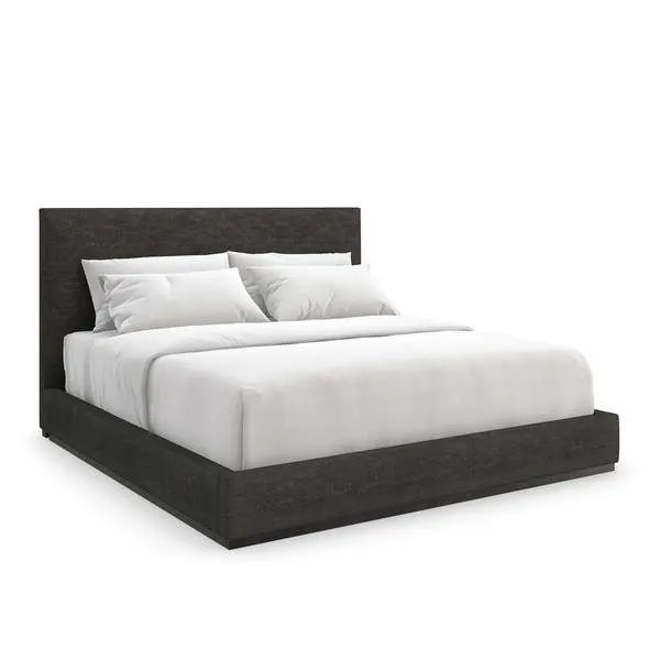 The Boutique Bed with tall cushioned headboard and low platform base in dark upholstery, with white bedding