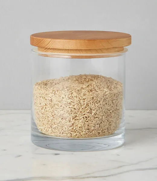 Close-up front view of a large natural wood top canister filled with rice on a marble surface