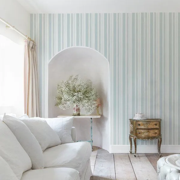 Wallpaper with delicate pastel blue and white watercolour vertical stripes in a bright, coastal style living room