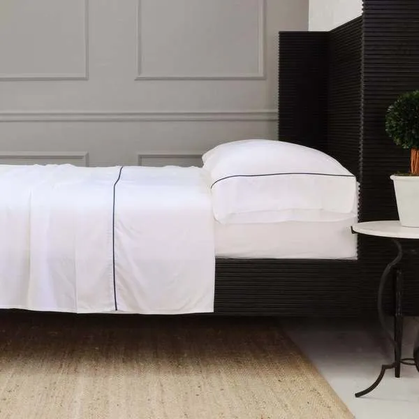 Set of two standard-size white pillowcases with navy blue trim in a modern bedroom setting