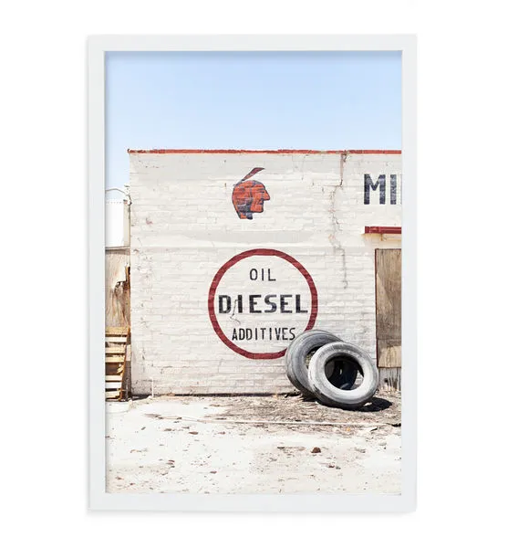 Aerial photo of a white brick wall with vintage red and black Route 66 signage, Indian head, and two tires against the wal...