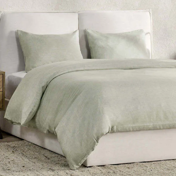 Sage green duvet set on a white upholstered bed with two matching pillow shams
