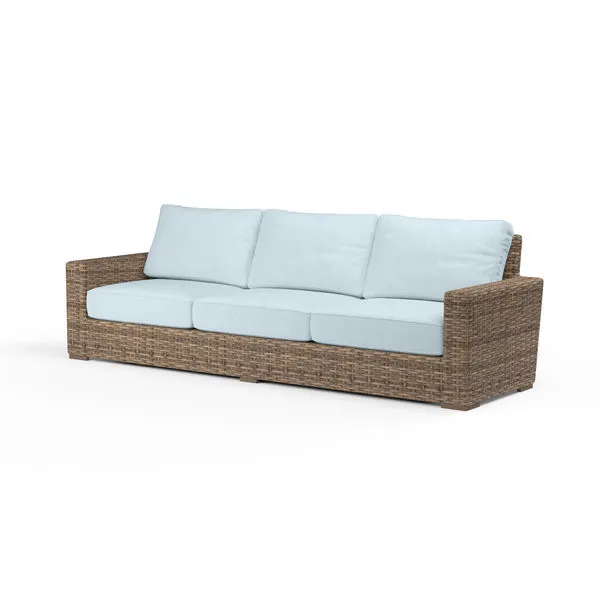 Outdoor Havana Sofa in weathered tobacco wicker with light blue tailored cushions, wide armrests, and low profile