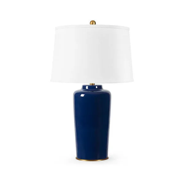 Table lamp with a glazed ceramic midnight blue base and a white drum shade topped with a brass finial