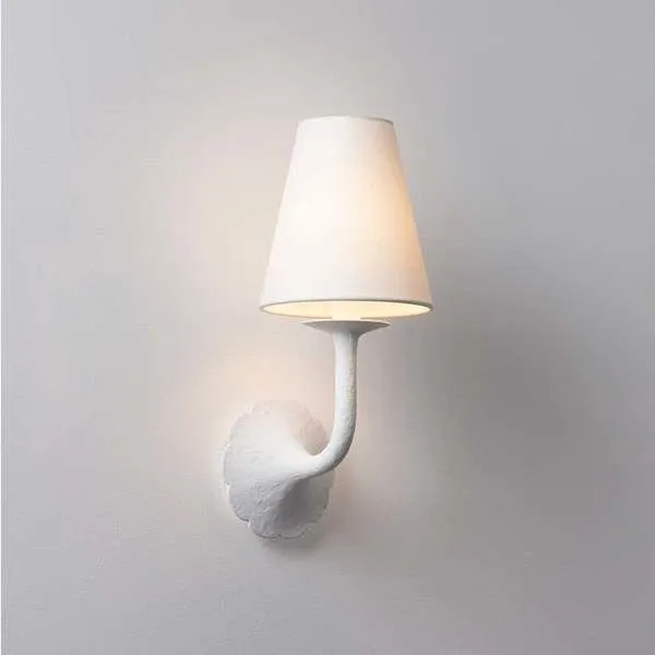 White Winnipeg Wall Sconce with scalloped floral backplate and tapered white linen shade lit softly against pale wall