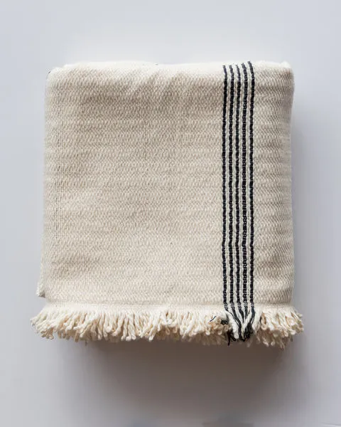 folded cotton throw with black stripe detail and fringed edges on light gray surface