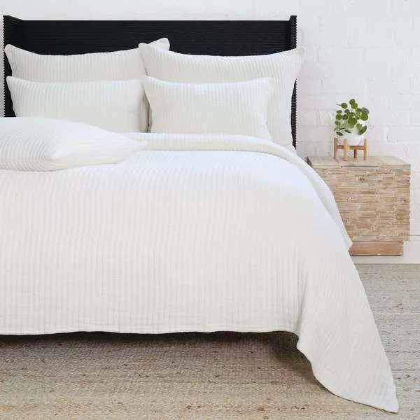Ivory Vancouver Oversized Throw with an interwoven stripe pattern draped on bed with matching pillows