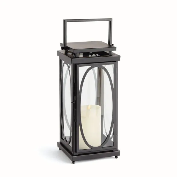 Tall black outdoor lantern with oval frames on glass panels and wide square base holding a white candle