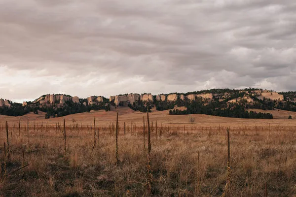 Wide landscape of Crazy Horse Country with dry grass foreground and rocky ridges under cloudy sky