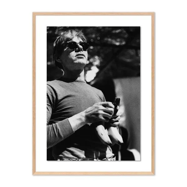 Black and white framed photograph of Andy Warhol holding a bunch of bananas wearing sunglasses
