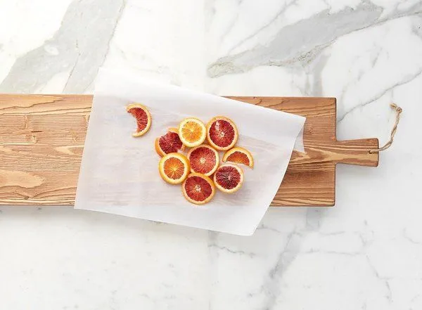 Top view showing light wood tone plank with sliced citrus fruits on parchment paper