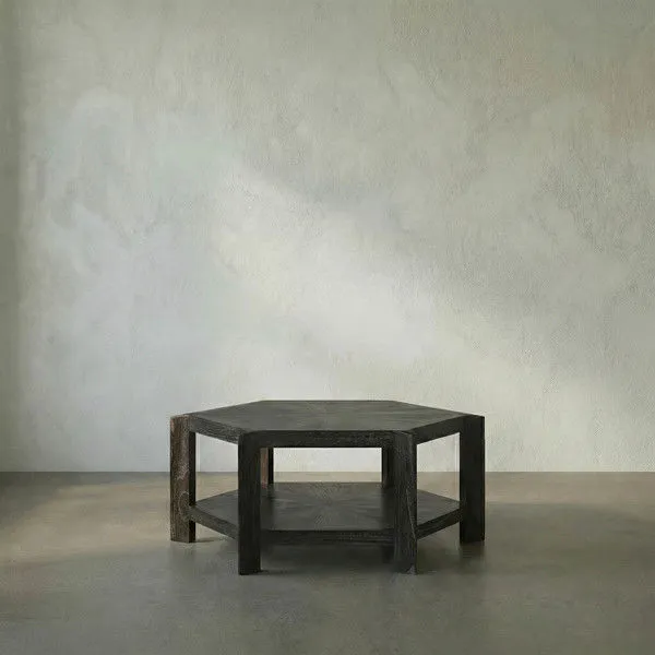 Hexagonal Yuhuda Coffee Table in cinder black mindi wood with lower shelf and thick legs, set against plain background