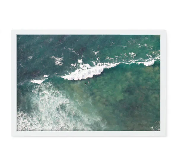 Aerial photograph of green-blue ocean waves with surfers paddling near the breaking surf