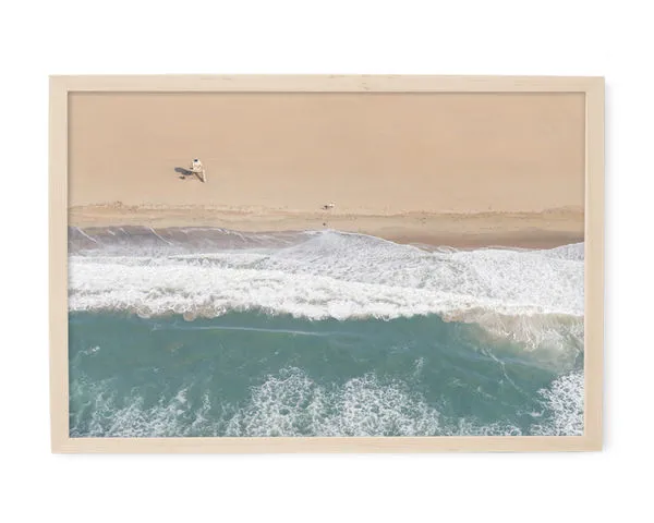 Aerial beach photography showing crashing waves on sandy shore with a lone surfboarder near the water's edge in a natural ...