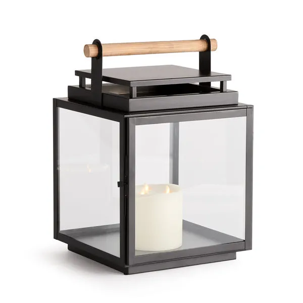Square outdoor lantern with wide glass panes, black metal frame, and a teak wood handle, containing a lit candle