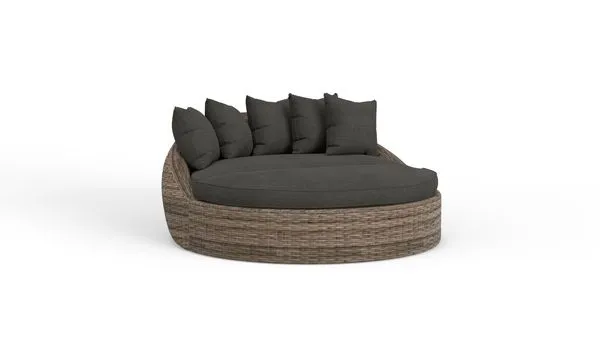 Round outdoor daybed with aged tobacco all-weather wicker frame and dark plush cushions and pillows