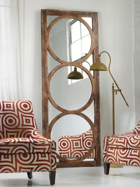 Tall floor mirror with a rustic wooden frame featuring three large circular cutouts, leaning against a white wall between ...